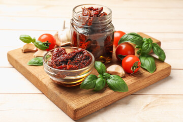 Delicious sun dried tomatoes, fresh vegetables, basil and garlic on white wooden table, closeup