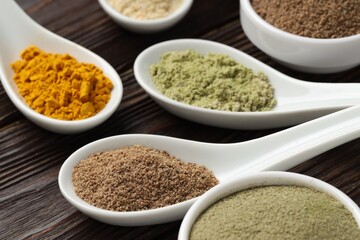 Different superfood powders in spoons on wooden table, closeup