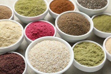 Different superfood powders in bowls on grey textured table, closeup
