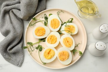Boiled eggs, microgreens and oil on white marble table, flat lay