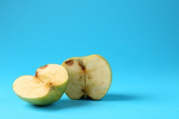 Halves of damaged apple on light blue background. Space for text