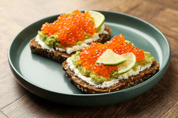 Delicious sandwiches with avocado, red caviar, cream cheese and lime on wooden table, closeup
