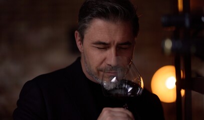 Middle aged man tasting, drinking wine in cellar. Wine expert rating a glass of red wine. Professional sommelier satisfied.