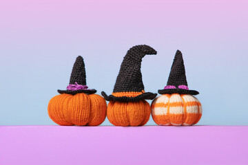Knitted orange pumpkins with black witch hat on purple podium and blue pink gradient background,...