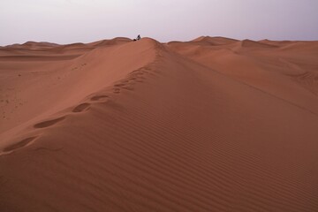 Group of people sitting on dune on Sahara desert, footprints in sand, Morocco