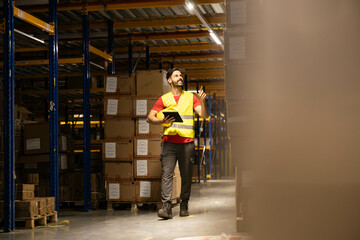 A warehouse worker with a tablet smiling while walking through an organized aisle filled with...