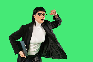 Professional woman in a black blazer hurries while holding a notebook under bright green background...