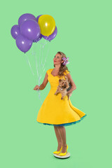 Woman in yellow dress holds balloons and dog against a green background at a playful outdoor event during warm weather