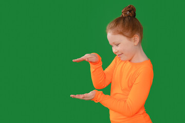 Young girl in  orange shirt showcases imaginary objects against a bright green background during a...