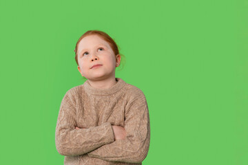 Child with red hair wearing a sweater looks up thoughtfully against a vibrant green background in a...