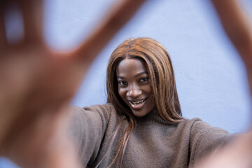Confident young Black woman taking a selfie with her hands framing her face.