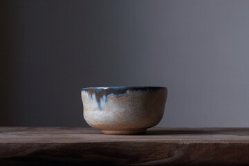 A handmade ceramic cup with blue glaze sits on a wooden table, bringing wabi-sabi aesthetics to a calm, minimalist setting.