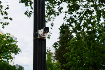 A surveillance camera monitors the area from a street pole surrounded by trees