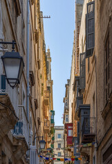 Fototapeta premium A view down an alleyway in Valletta old city, Malta, with traditional houses, bay windows and colourful shutters.