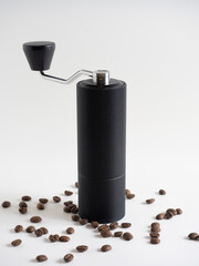manual coffee grinder black on a white background. There are coffee beans nearby.