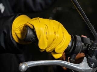 Close-up of biker in yellow leather gloves holding motorcycle handlebars.