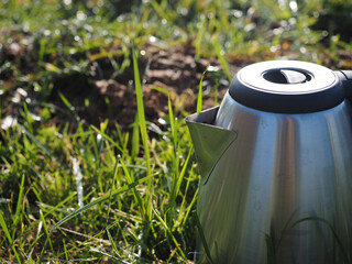 Close-up of a metal electric kettle standing on green grass