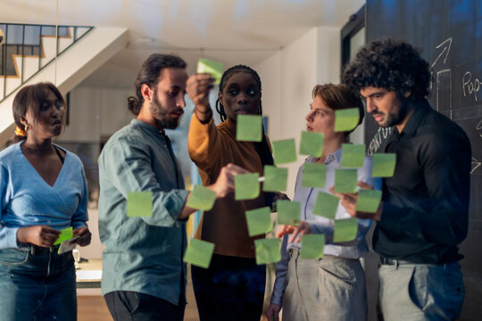 Businesspeople planning strategy using adhesive notes on glass wall in office