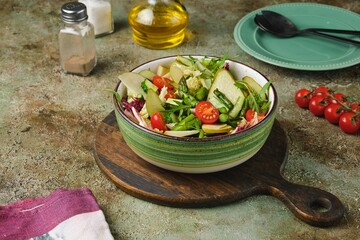 Fresh vegetable salad with fried asparagus, arugula, cucumber and cherry tomatoes in a green salad bowl on a green concrete background. Vegetable salads.