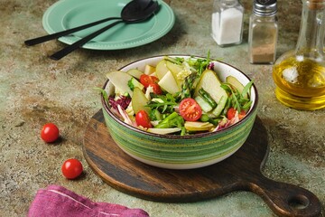 Fresh vegetable salad with fried asparagus, arugula, cucumber and cherry tomatoes in a green salad bowl on a green concrete background. Vegetable salads.