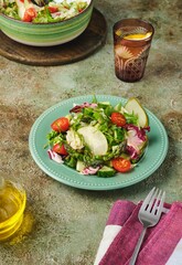 Fresh vegetable salad with fried asparagus, arugula, cucumber and cherry tomatoes on a green plate on a green concrete background. Vegetable salads, vegan recipes. Seasonal vegetables.