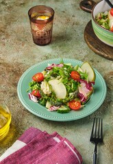 Fresh vegetable salad with fried asparagus, arugula, cucumber and cherry tomatoes on a green plate on a green concrete background. Vegetable salads, vegan recipes. Seasonal vegetables.