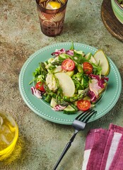 Fresh vegetable salad with fried asparagus, arugula, cucumber and cherry tomatoes on a green plate on a green concrete background. Vegetable salads, vegan recipes. Seasonal vegetables.
