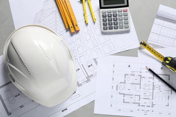 Flat lay composition with different architectural drawings and hard hat on gray table