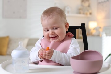 Cute little baby eating on feeding chair at home