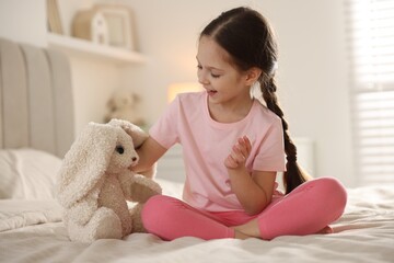 Cute girl with toy bunny on bed at home