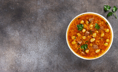 Traditional Moroccan harira soup with chickpeas, beef, parsley and spices on grey background. Copy space. Top view.