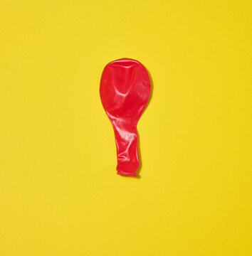 One red deflated balloon lies on a yellow background.