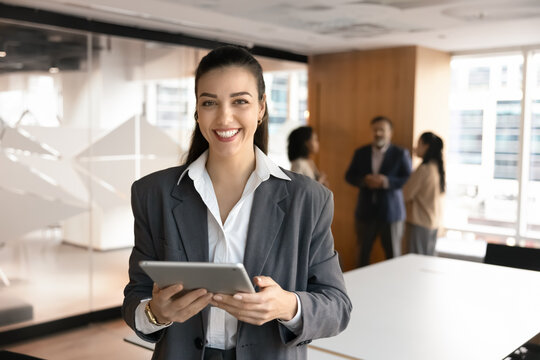 Portrait of young professional businesswoman, corporate trainer or project coordinator posing in meeting room with digital tablet, look at camera, preparing for meeting or presenting data to teammates