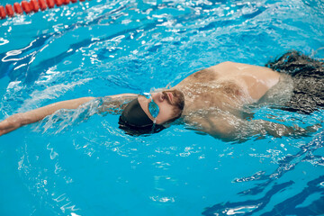 Man in black swimming cap swimming backstroke in the pool