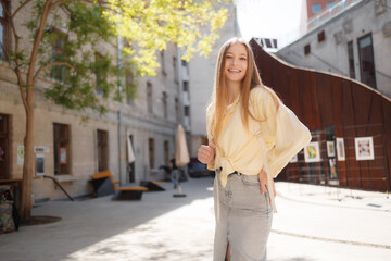 Fototapeta premium Young woman enjoys sunny day in urban courtyard while smiling and wearing casual outfit with backpack