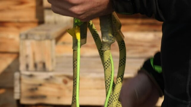 Close-up shot: hand securely clips a metal carabiner onto a D-ring of a yellow and black safety harness. Essential for climbing, adventure, and fall protection.