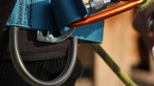 Close-up shot: hand securely clips a metal carabiner onto a D-ring of a yellow and black safety harness. Essential for climbing, adventure, and fall protection.
