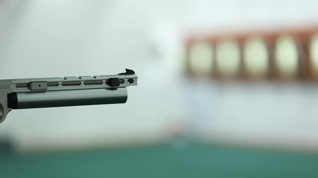 Close-up of a Sport air pistol firing, a puff of smoke visible from its silver barrel. Focus on precision against a blurred shooting range background. Perfect for marksmanship.