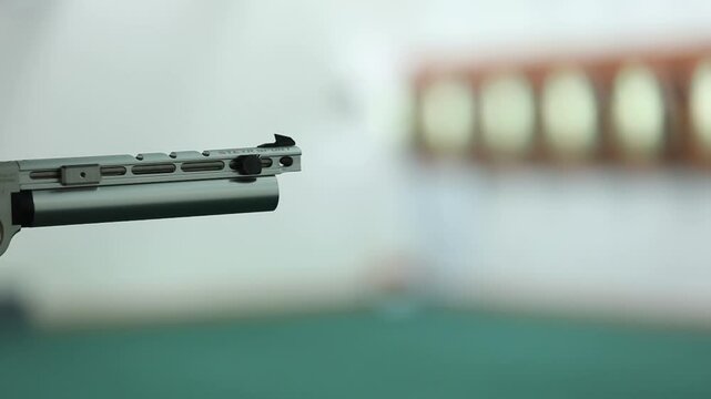 Close-up of a Sport air pistol firing, a puff of smoke visible from its silver barrel. Focus on precision against a blurred shooting range background. Perfect for marksmanship.