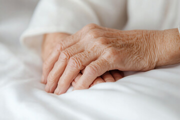 Two aged hands gently clasped on a cozy white blanket, reflecting a moment of tranquility and warmth, perhaps in a home environment during daytime