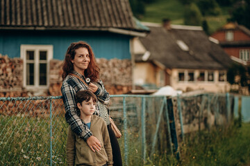 A young woman and her son stand near a house in a mountain village in summer. Summer travel along mountain routes in Europe.