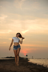 Fototapeta premium A beautiful young smiling blonde in a lacy white short top and u denim shorts