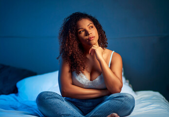 Obraz premium Young attractive woman, sitting on bed before going to bed, thinking about what to do, bored