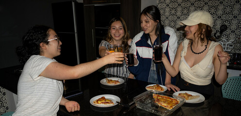 A group of friends share joyful moments indoors, enjoying drinks and delicious pizza for dinner. The atmosphere reflects companionship, happiness