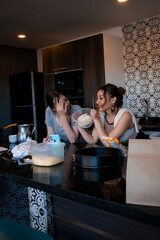 Two female friends laughing and preparing pastries in a well-decorated kitchen. Showing it to smartphone for social media.The scene conveys warmth, friendship, and creativity