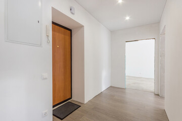 The bright empty hall of the apartment with a brown entrance door and unfinished repairs. Laminated floor. Unfurnished.