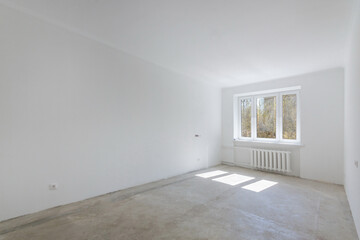 An empty bright room with a window and unfinished repairs. The floor is without finishing. Unfurnished.