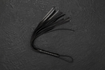Black whip on concrete background, top view. BDSM concept