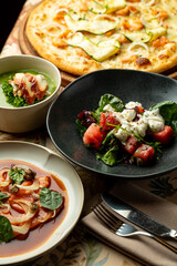 A beautifully arranged table displays a variety of appetizing dishes, including a creamy soup, refreshing salad, and a savory pizza, highlighting the artistry of contemporary dining