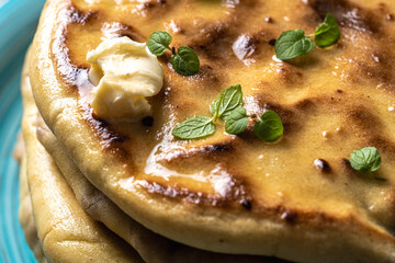 Khychins, traditional Caucasian, Eastern dish. Flatbread stuffed with minced meat with sauce on a turquoise plate with cutlery and a napkin on a wooden table. Close-up.
